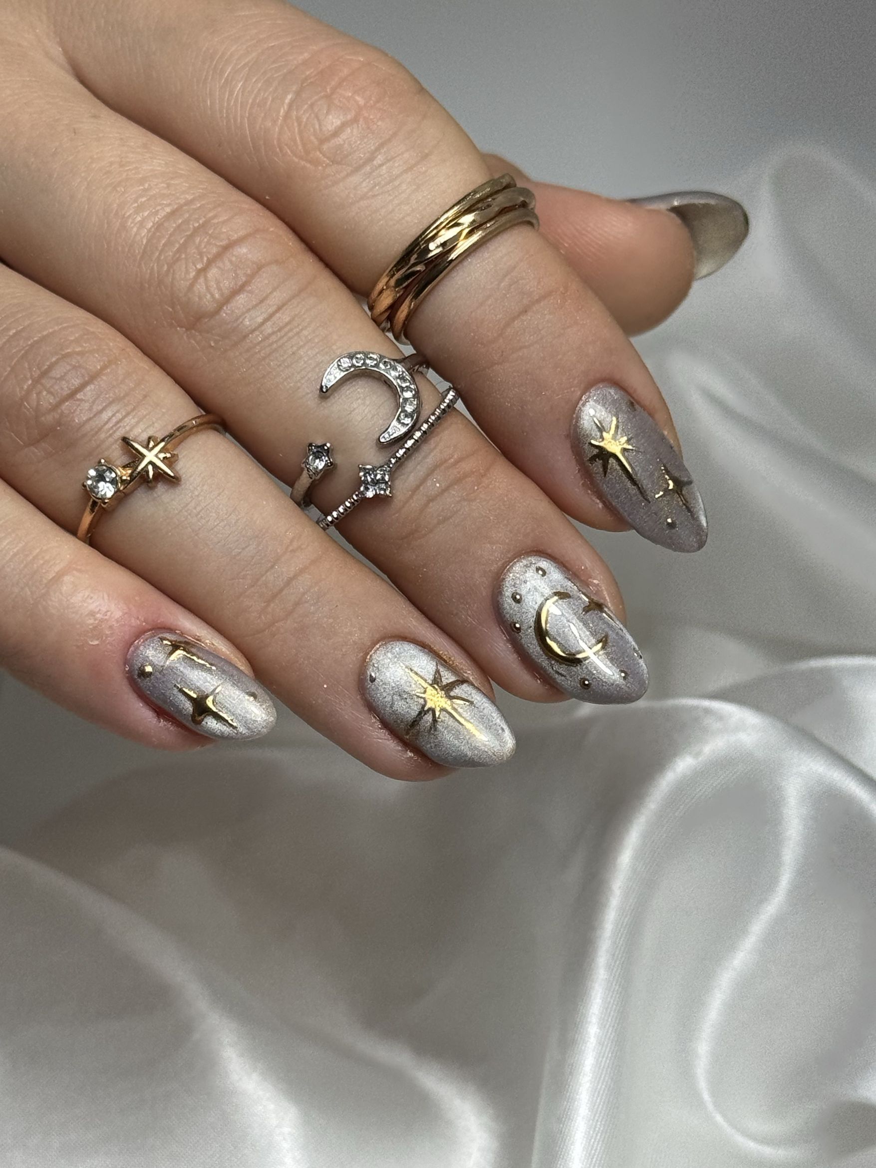 Manicura plateada con motivos de luna y estrellas doradas